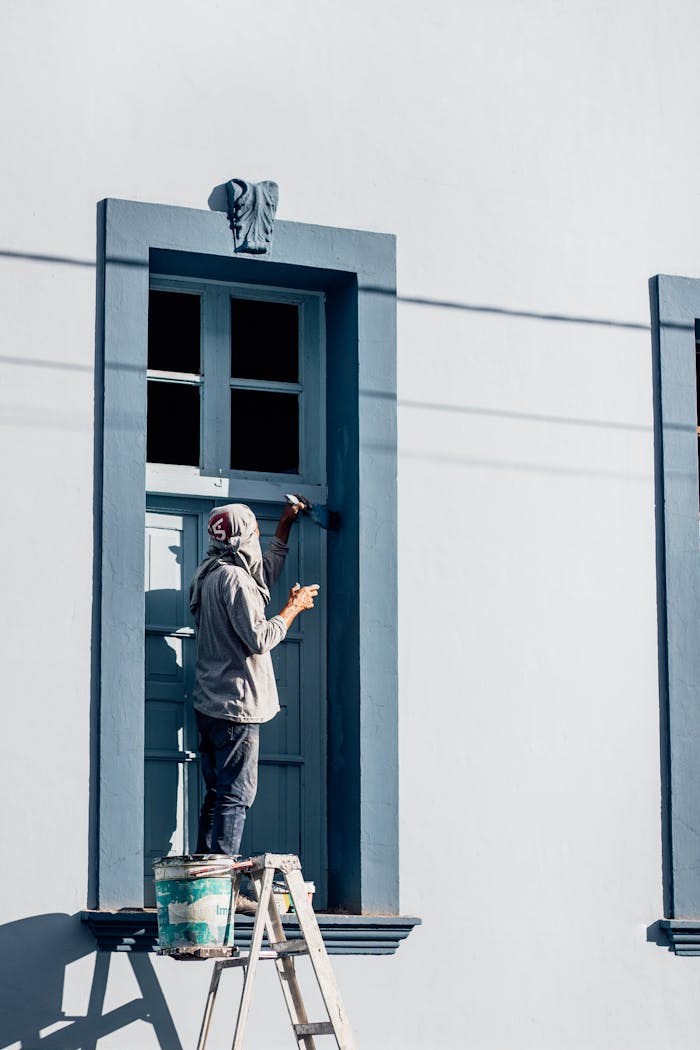 Man on ladder painting a blue window frame on a sunny day in Yurimaguas, Peru