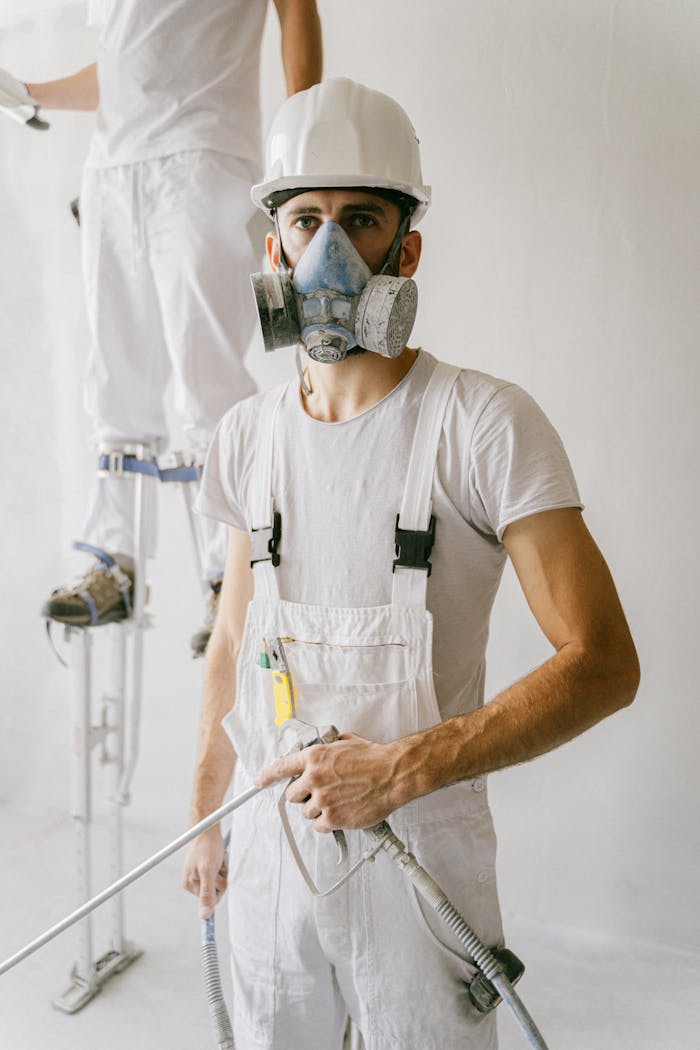 A focused construction worker wearing safety gear including a hard hat and gas mask indoors.